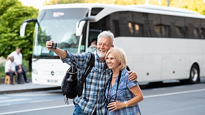 Mehrtages- und Wochenendreisen, ein Paar fotografiert sich vor einem Bus.