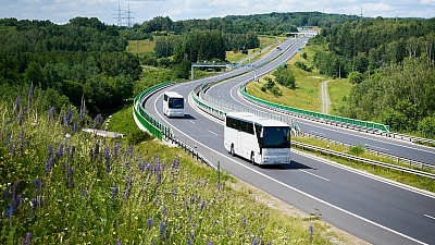Zwei Reisebusse auf Landstraße in grüner Hügellandschaft – unterwegs auf großer Fahrt bei bestem Wetter